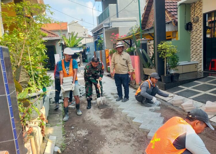 Tanggalkan Senjata, Babinsa Manyar Bantu Warga Pasang Paving Blok Dukung Pembangunan Jalan Desa